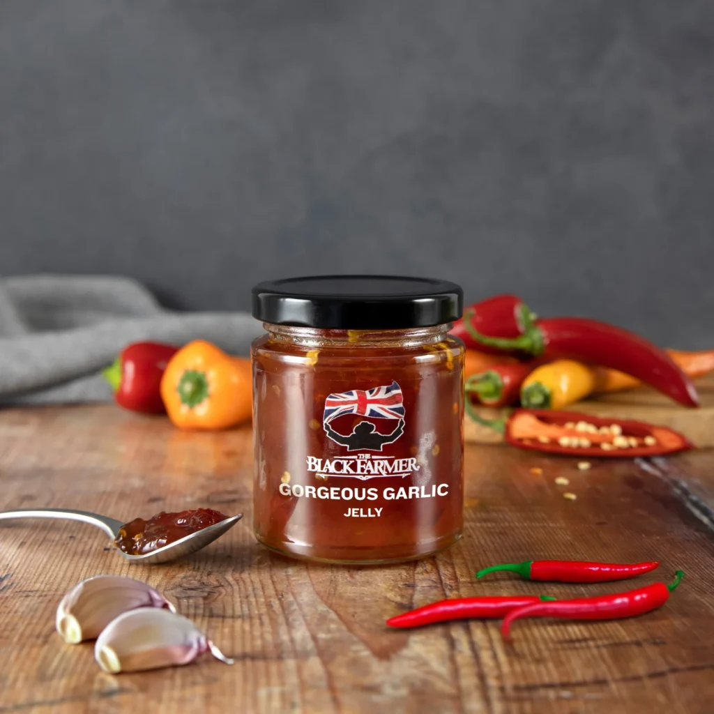 A jar of The Black Farmer’s Gorgeous Garlic Jelly, showcasing a golden jelly with a garlic bulb illustration on the label.