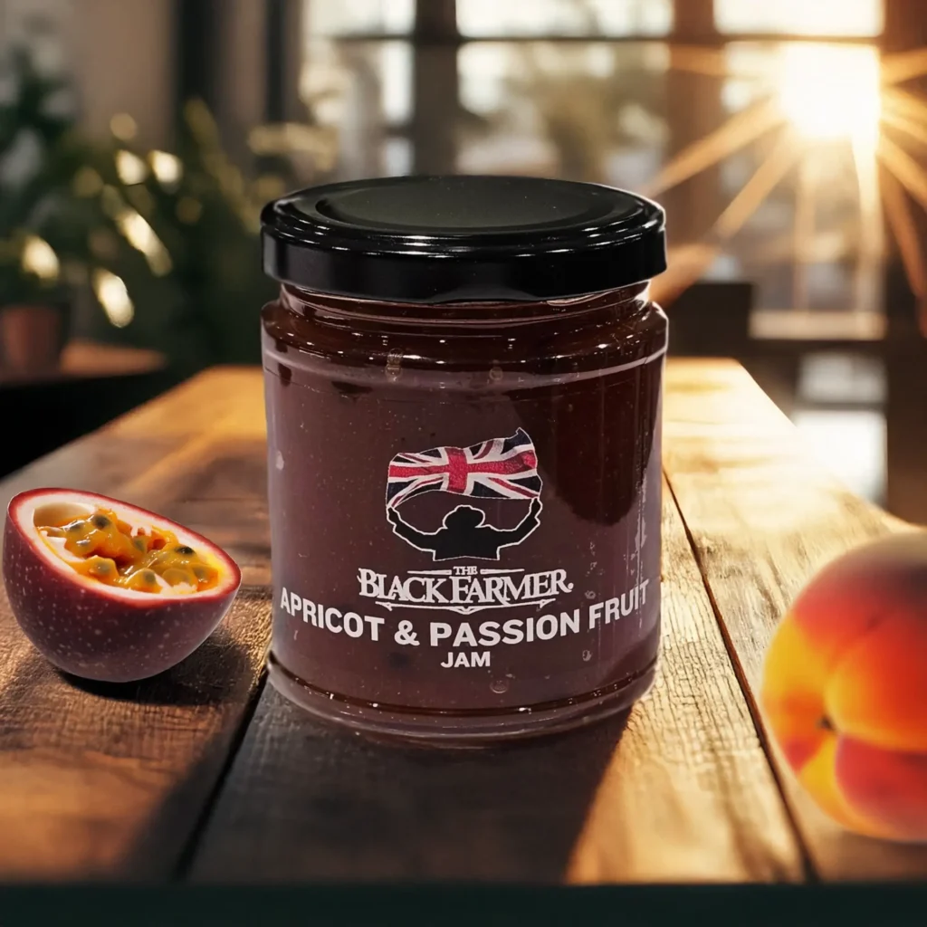 A jar of The Black Farmer Apricot & Passion Fruit Jam placed on a wooden table with fresh apricots and passion fruit in the background, illuminated by warm sunlight.