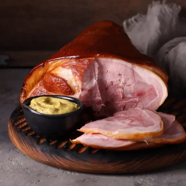 A succulent smoked ham hock, sliced and accompanied by a bowl of mustard, displayed on a wooden board for a rustic touch.