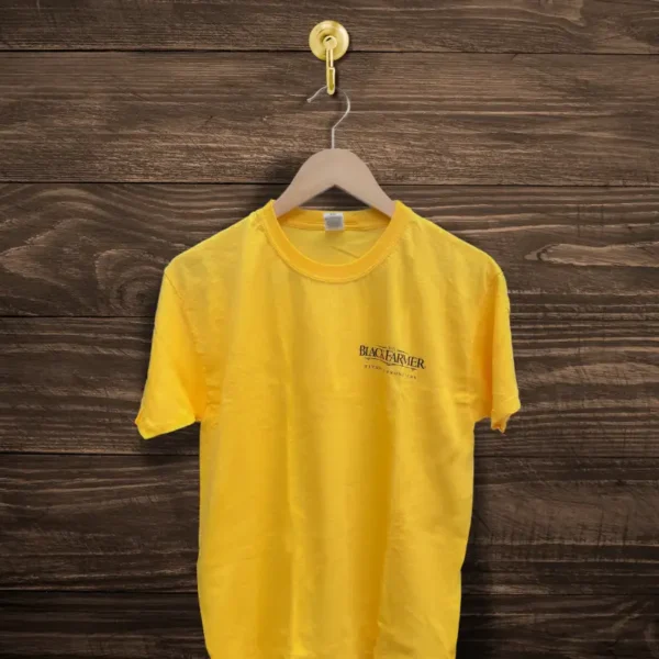 The Black Farmer yellow t-shirt with a classic crew-neck design and embroidered logo, displayed on a hanger against a wooden background.